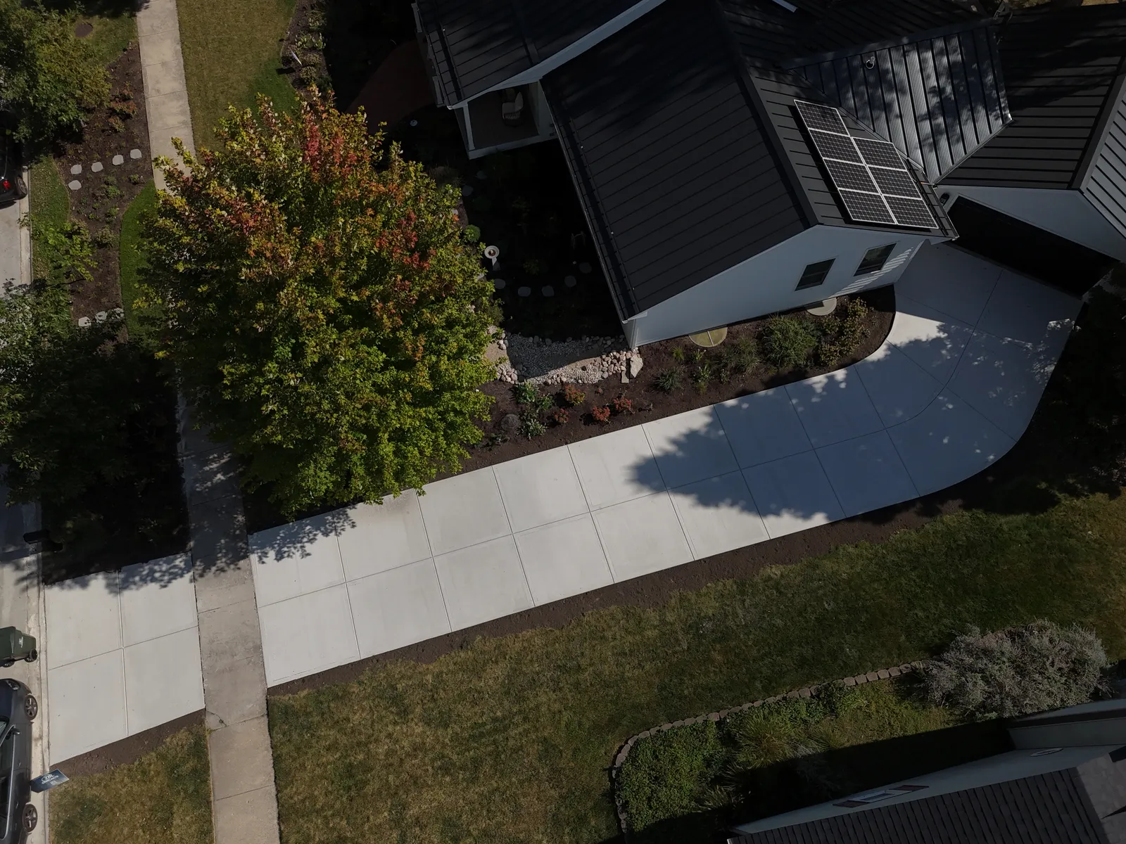 Sweeping concrete walkway at modern dark-roofed home — aerial