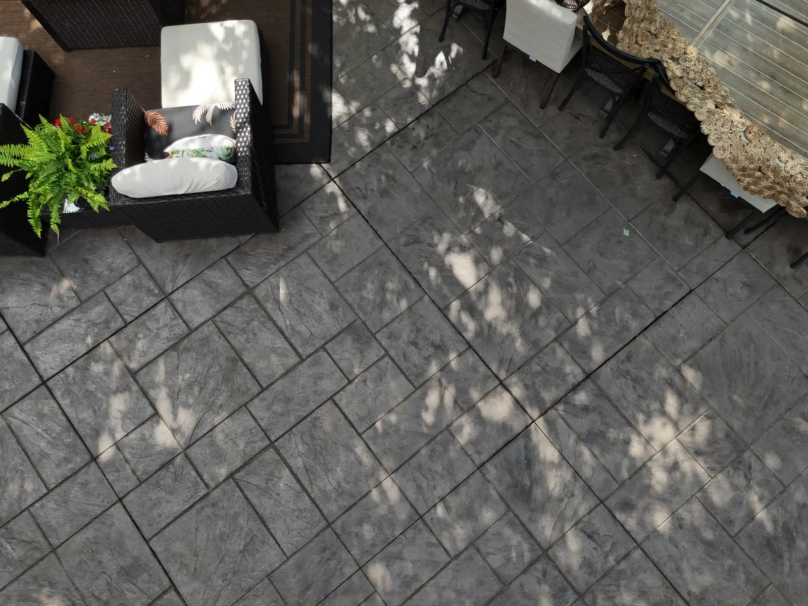 Dark gray stamped patio with outdoor furniture in dappled sunlight